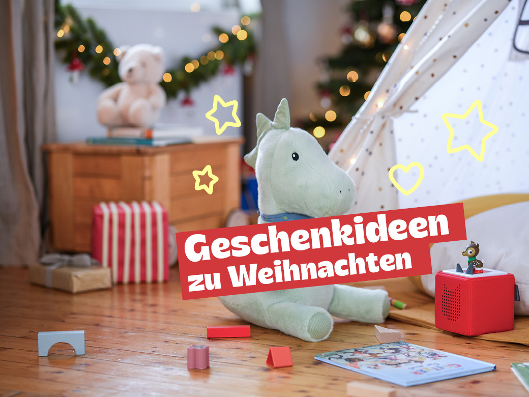 Geschenkideen zu Weihnachtn: Kuscheldrache, tonie Box, Bausteine und Buch abgebildet. Im Hintergrund eine Lichterkette und Tannengrün.
