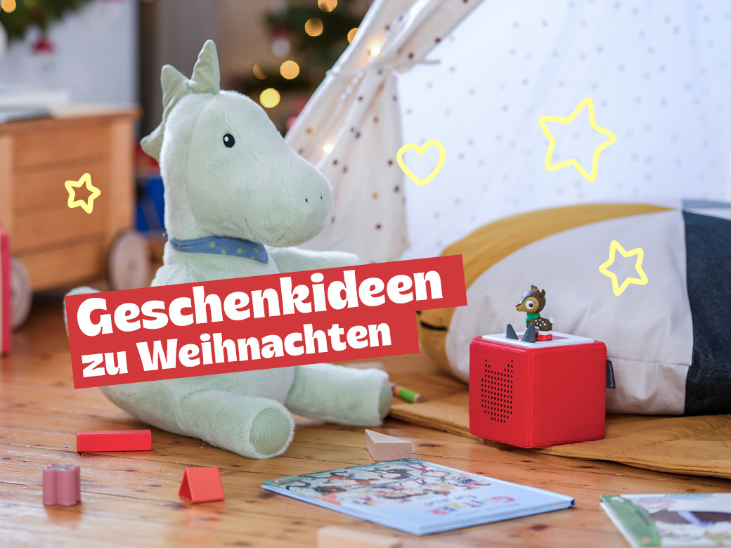Geschenkideen zu Weihnachtn: Kuscheldrache, tonie Box, Bausteine und Buch abgebildet. Im Hintergrund eine Lichterkette und Tannengrün.
