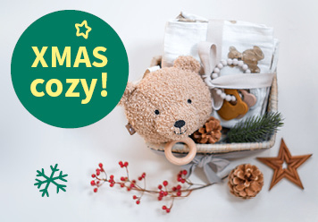 XMAS-cozy: Spieluhr, Schnullerkette und Mullwindeln liegend zwischen Sternen und Tannenzapfen abgebildet.
