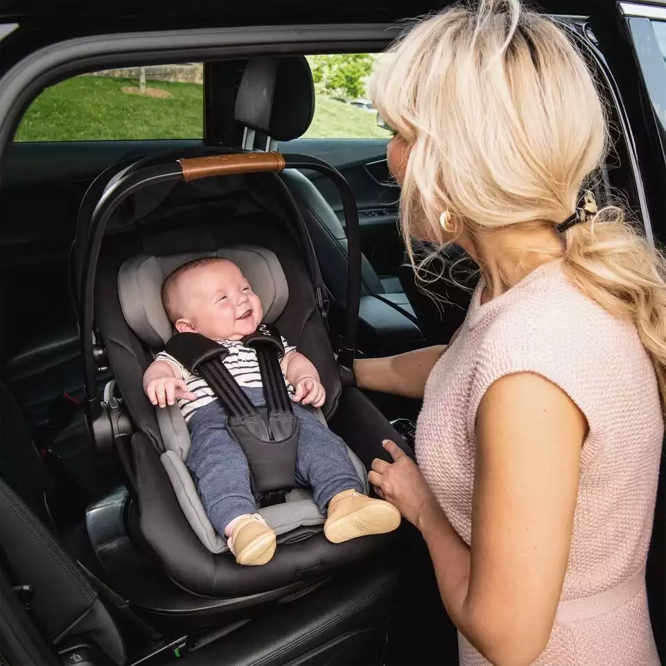 Eine frau, die ein baby auf einem autositz hält.