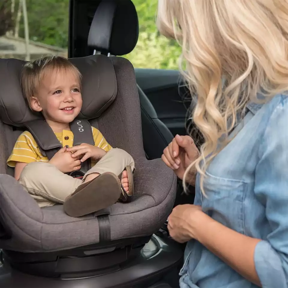 Eine frau, die ein kind auf einem autositz hält.